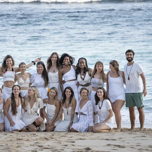 Group of 200-hour yoga teacher training students gathered in white on the beach after graduation.