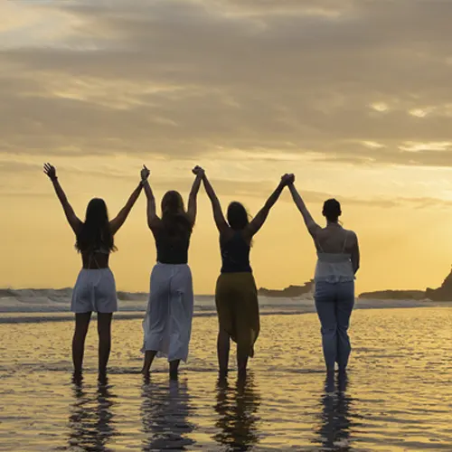Four yoga students holding hands at sunset during 200-hour yoga teacher training.