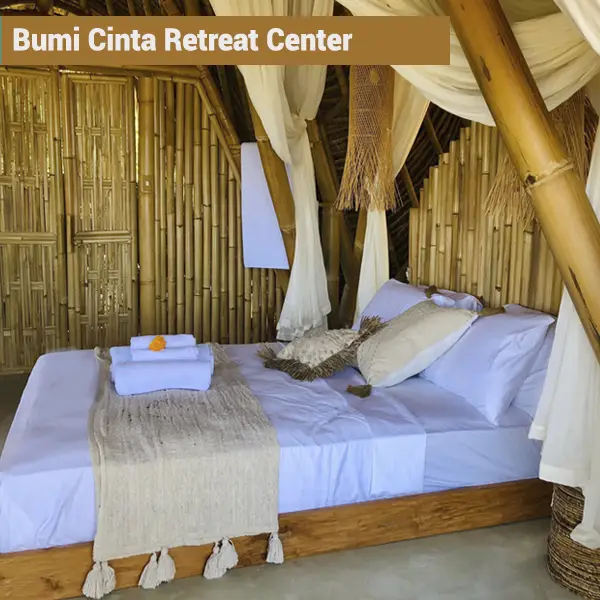 Interior of a bamboo hut with white canopy bed at Bumi Cinta retreat center in Bali