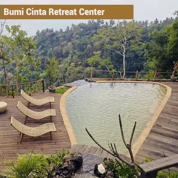 Natural swimming pool with jungle valley views and wooden lounge chairs at Bumi Cinta retreat center in Bali